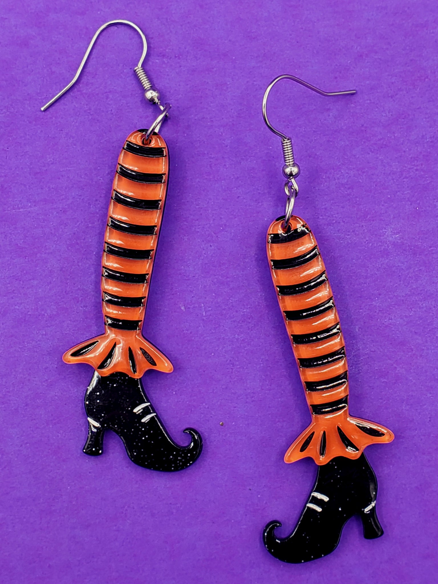 pair of resin dangle earrings in the shape of striped black and orange legs with black glittery pointed toe witchy boots