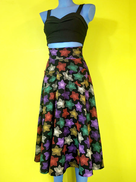 stretch cotton knit high-waisted midi length skirt in a multicolored blooming tropical flower print on a black background and featuring a 3" wide waistband and heart-shaped patch pockets. shown on a blue mannequin.