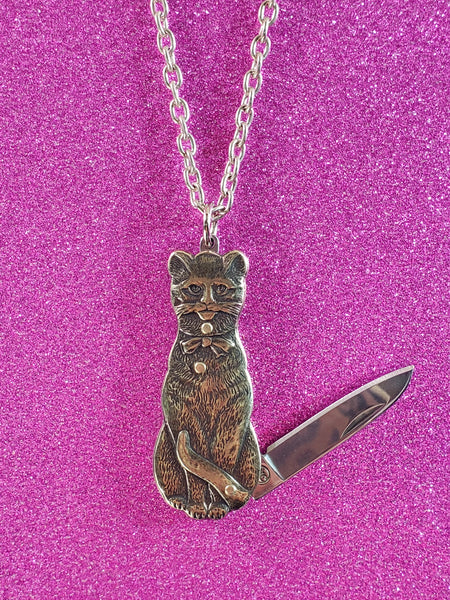 Mini pocket knife charm in the shape of a cat with antiqued brass finish. On a 20” silver metal link chain. showing close up of pendant partially opened with knife visible 