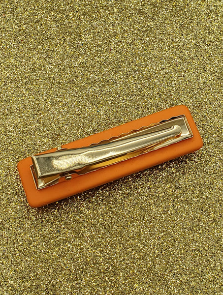 bright orange rectangular shaped hair clip with a matte soft touch finish, adorned with round gold bead embellishments and multicolored faceted rhinestones, showing the back with gold metal gator clip fastener