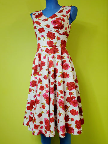 a sleeveless fit and flare dress in a stretch cotton knit creamy white background blooming pink, red, and green rose pattern, and featuring a faux-wrap surplice bodice with v-neckline, and paneled just-below-the-knee length full skirt. shown on a mannequin