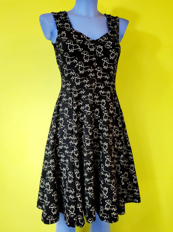 sleeveless stretch cotton knit flared knee length dress with sweetheart neckline in a cream print repeat pattern of dachshunds against a black background. shown worn by a mannequin