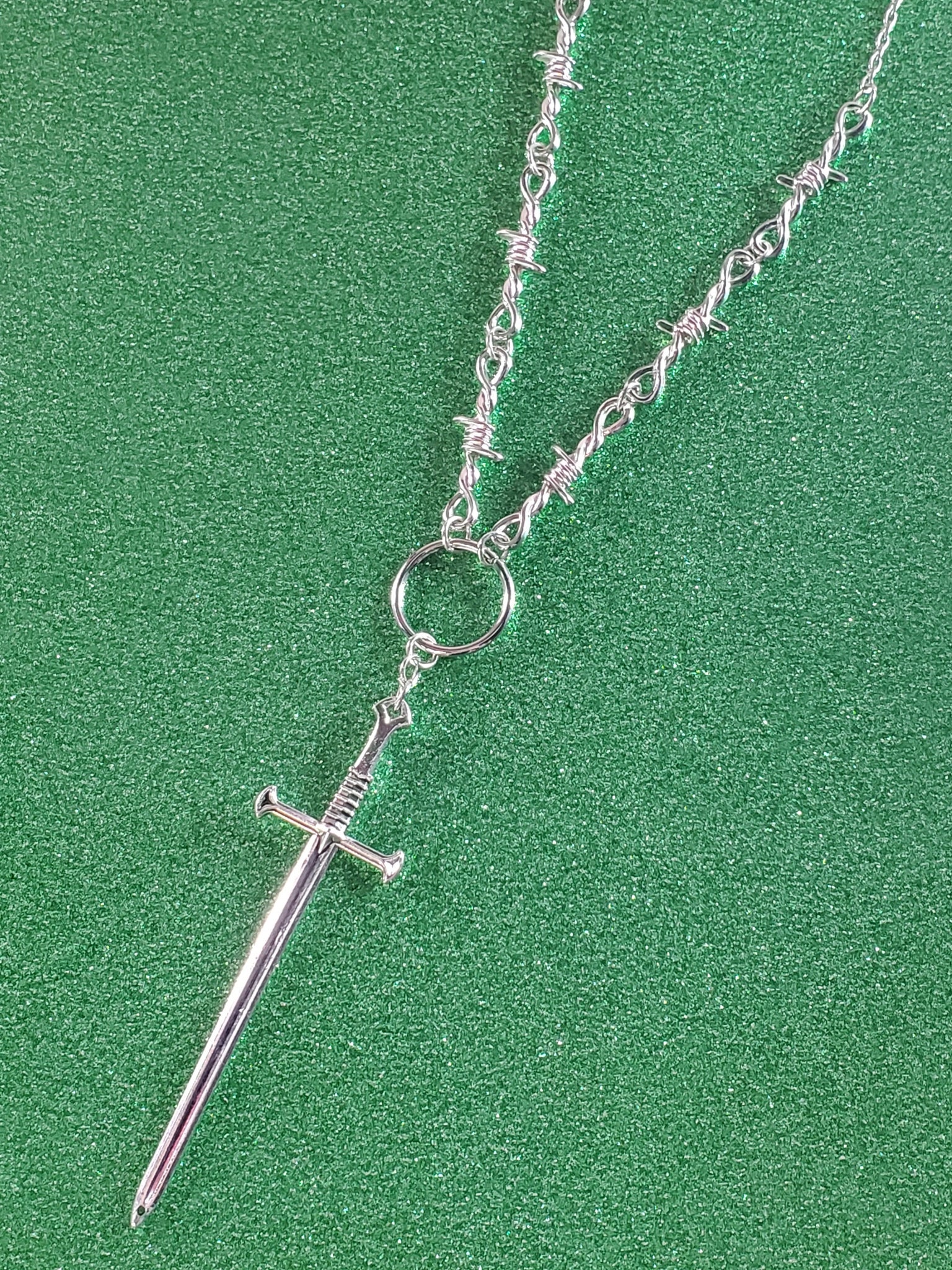 24” silver metal barbed wire necklace with a sword charm connected by a metal o ring. showing close up view of pendant