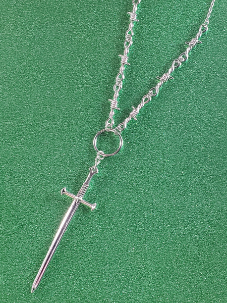 24” silver metal barbed wire necklace with a sword charm connected by a metal o ring. showing close up view of pendant