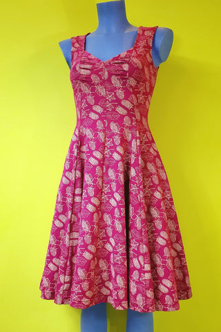 sleeveless stretch cotton knit dress in a cream colored repeat pattern of leaves and Olallieberries on a magenta background, and features a sweetheart neckline, fitted bodice with lightly gathered at the bust, vertical seaming, and a full swingy knee length skirt