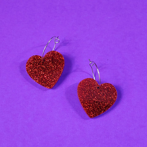 sparkly pair of red glitter heart-shaped acrylic resin charm hanging from a delicate silver plated hoop earrings
