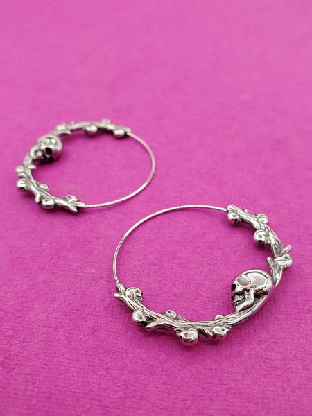 stainless steel infinity closure hoop earrings with skull and branch detail at the bottom of each hoop with tiny skulls growing out of each branch. 