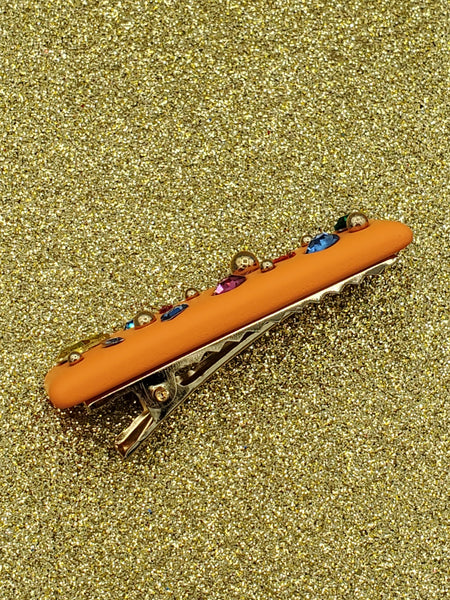 bright orange rectangular shaped hair clip with a matte soft touch finish, adorned with round gold bead embellishments and multicolored faceted rhinestones. shown from the side with view of gold metal gator clip fastener