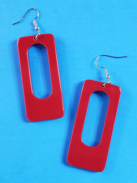 A pair of rectangular acrylic dangle earrings with rounded corners and an oblong hole in the middle. The front of the earring is deep red and the back is black