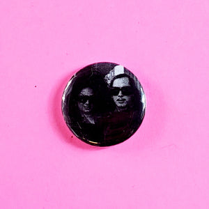black and white photo of John Waters (sporting long hair!) with his muse and often lead actress Divine on a 1” round pinback button