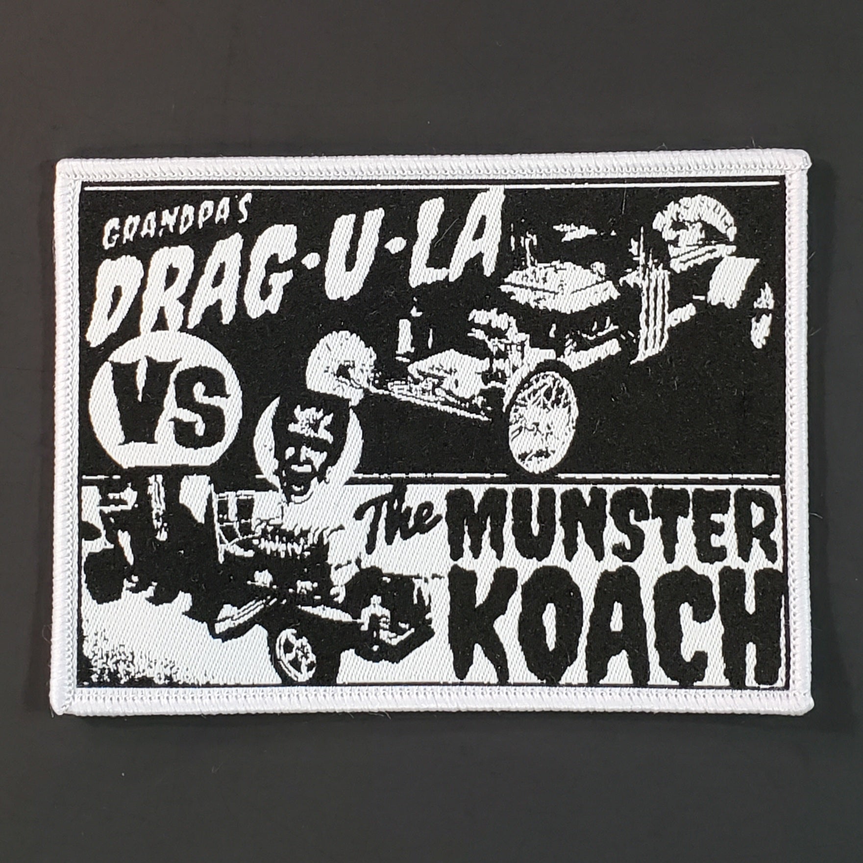 Black and white woven rectangular patch with embroidered white border featuring dragula and Munster Koach