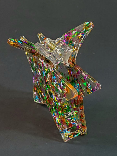 3 1/2” claw style clear acrylic with star-shaped multicolor glitter hair clip in the shape of a pointy star. Shown from the side.