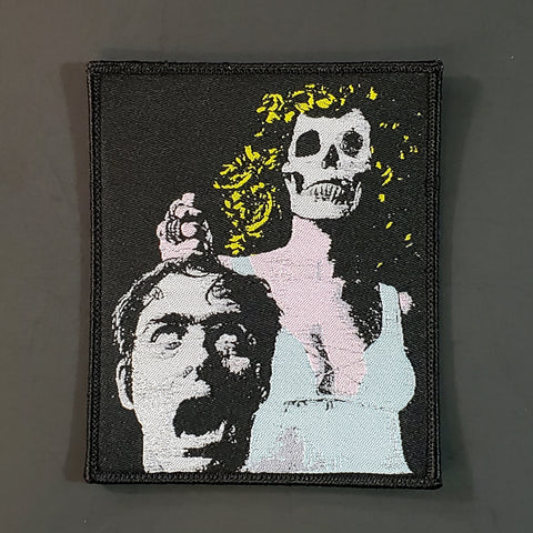 Rectangular black, pink, yellow, and grey woven patch with poster art from the movie The Night Evelyn Came Out of the Grave featuring a zombie woman with a skull head holding the screaming severed head of a man