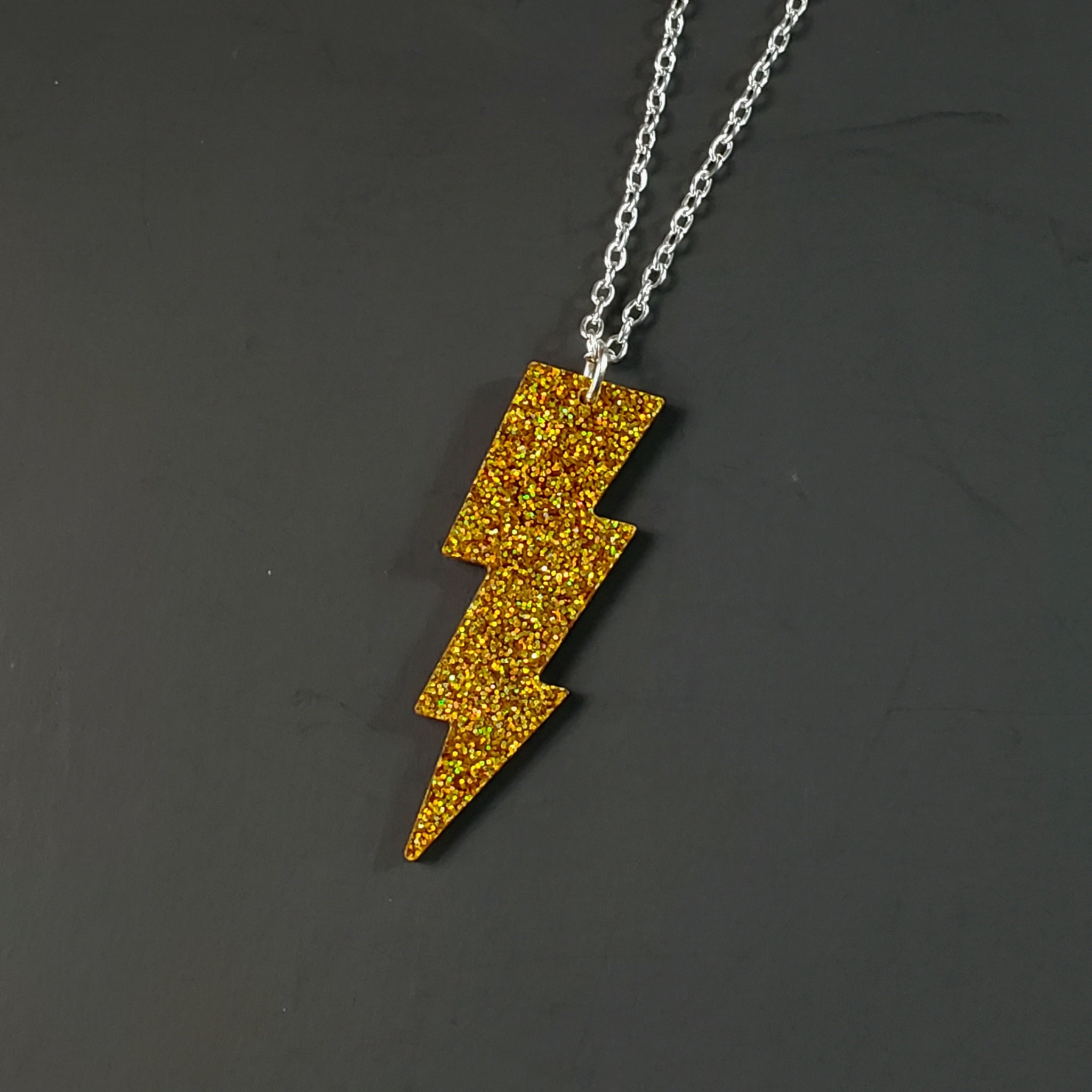 sparkly gold glitter lightning bolt shaped acrylic resin pendant attached to a silver plated curb style chain
