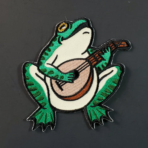 Embroidered patch of a green bullfrog playing a lute and singing