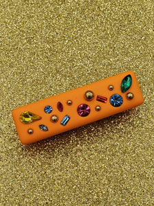 bright orange rectangular shaped hair clip with a matte soft touch finish, adorned with round gold bead embellishments and multicolored faceted rhinestones