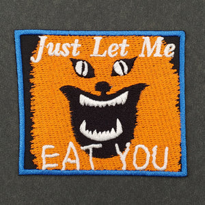 twill embroidered patch of orange cat Blanche from the movie House with caption in white "Just Let Me EAT YOU" on black background with blue border