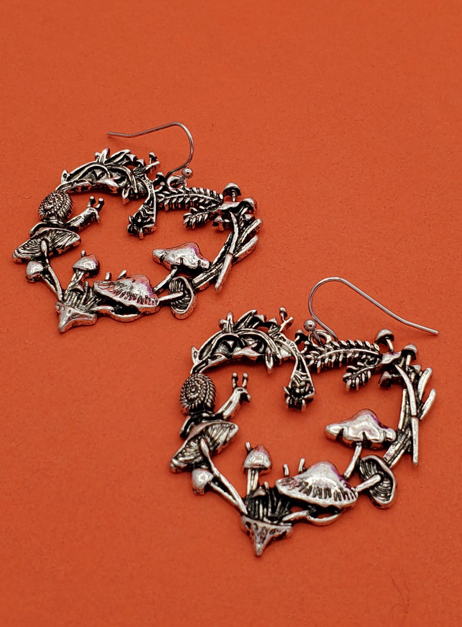 silver metal dangle earrings with charms in the shape of hearts made of mushrooms, snails, and leaves