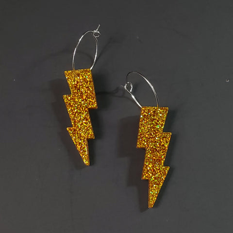 sparkly pair of gold glitter lightning bolt shaped acrylic resin charm hanging from a delicate silver plated hoop earrings