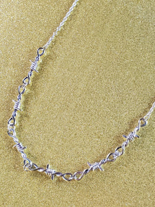 18” silver metal link chain necklace with connected pieces of barbed wire, shown close up.