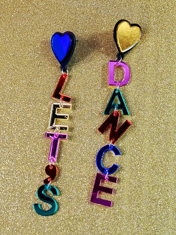 A pair of drop earrings made of mirrored acrylic letters attached to each other with jump rings spelling “LET’S” and “DANCE” in pink, green, yellow, blue, and red. Attaches to ear with heart shaped charm