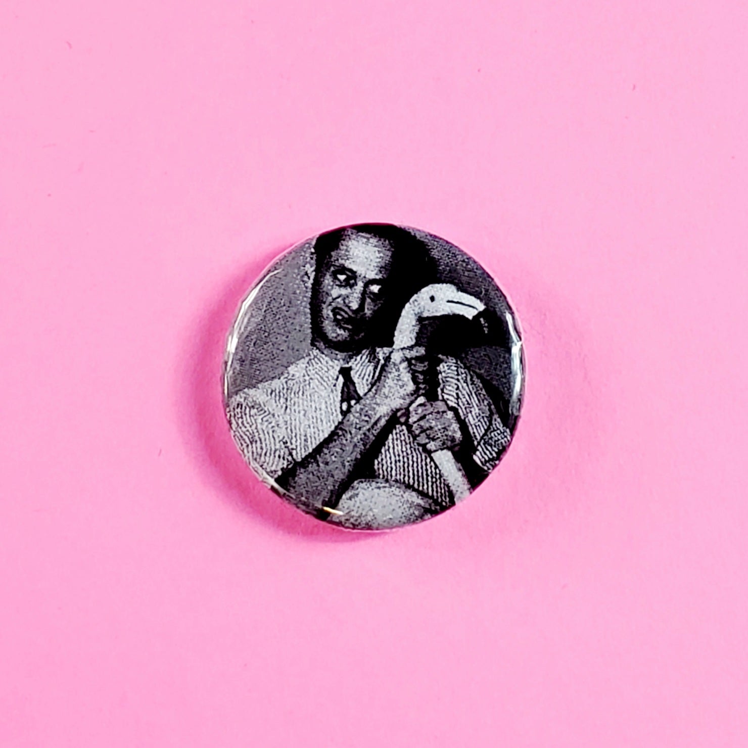 black and white photo of the Pope of Trash himself, John Waters, wrapping his hands around the neck of a (presumably pink) plastic flamingo on a 1” round pinback button