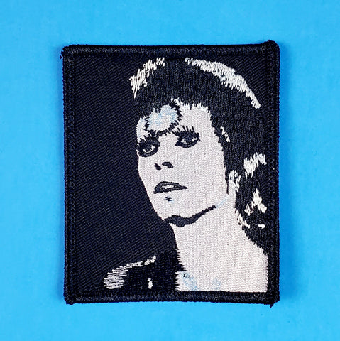 A rectangular embroidered patch of a classic Ziggy Stardust Mick Rock portrait in stark black & white with silver highlights.

