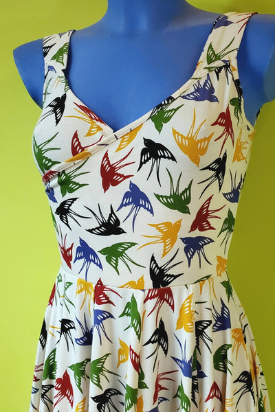 mannequin wearing a sleeveless fit & flare stretch cotton knit dress in creamy beige background print with repeating pattern of graceful flying swallows in black, red, blue, yellow, and green, and features a faux-wrap surplice bodice with v-neckline, wide straps, and mid-calf length extra full & swing-y paneled skirt. showing close up of bodice only