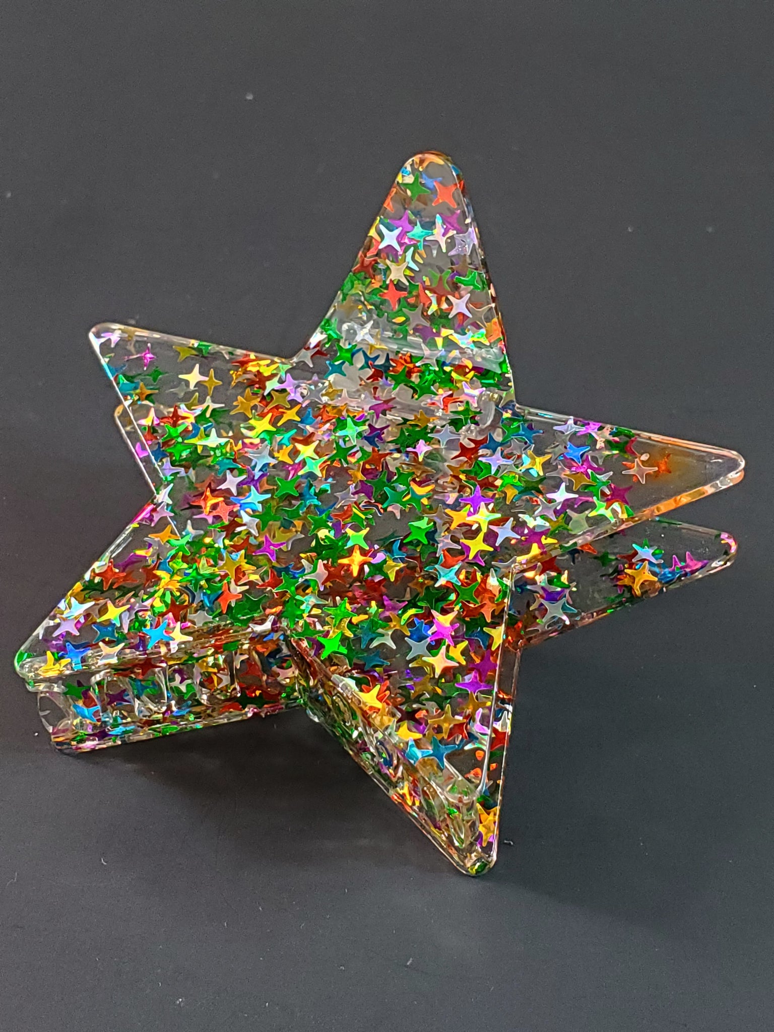 3 1/2” claw style clear acrylic with star-shaped multicolor glitter hair clip in the shape of a pointy star