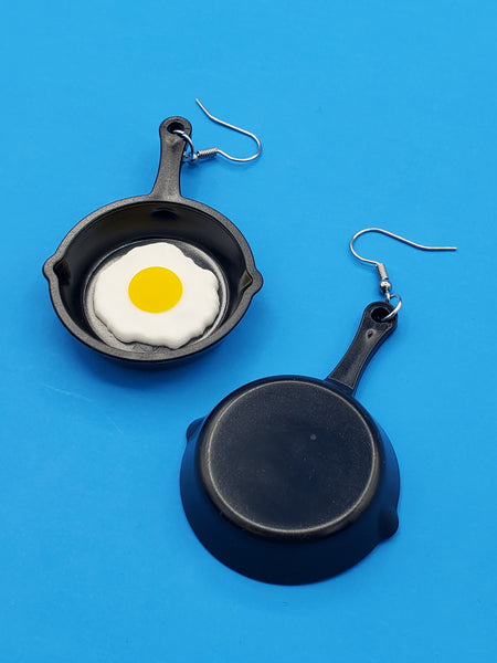 pair of dangle earrings with charms in the shape of cast iron frying pans with sunny side up eggs in each pan, showing the back view of one