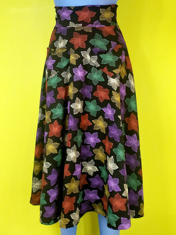 stretch cotton knit high-waisted midi length skirt in a multicolored blooming tropical flower print on a black background and featuring a 3" wide waistband and heart-shaped patch pockets. shown on a blue mannequin.