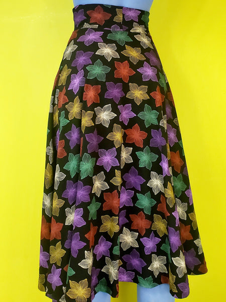 stretch cotton knit high-waisted midi length skirt in a multicolored blooming tropical flower print on a black background and featuring a 3" wide waistband and heart-shaped patch pockets. shown back view on a blue mannequin.