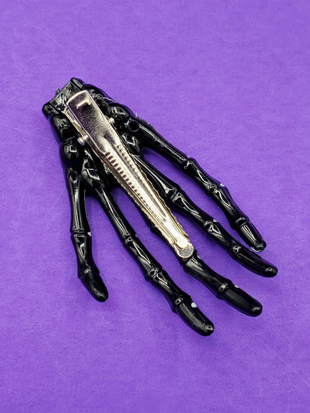 black plastic with white painted details skeleton hand hair clip, showing back view with silver metal gator clip fastener