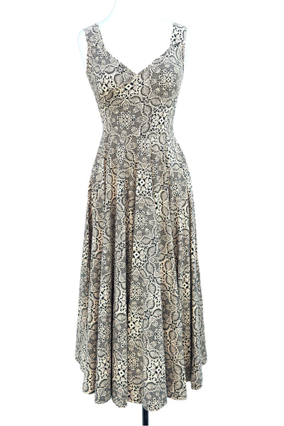 sleeveless fit & flare stretch cotton knit dress in creamy beige background print with repeating pattern of black floral lace and features a faux-wrap surplice bodice with v-neckline, wide straps, and mid-calf length extra full & swing-y paneled skirt. Shown on dress form