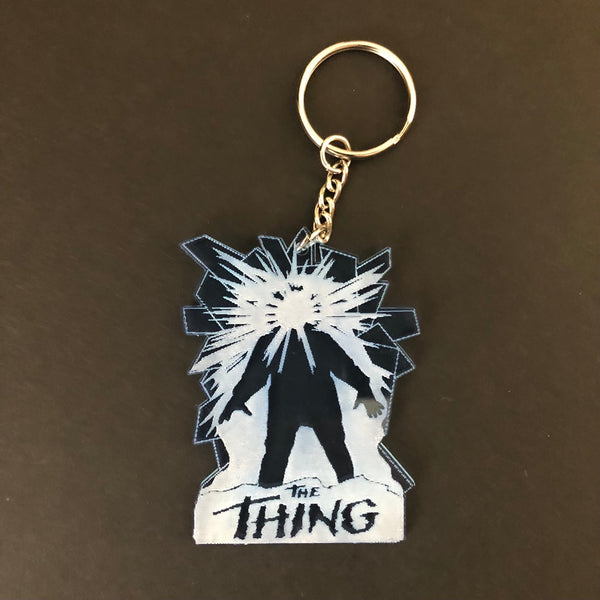 Laser-cut light blue acrylic keychain with etched detail of movie poster for The Thing shown on black background