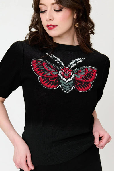 Model wearing black knit pullover sweater with round neckline, slightly puffed balloon short sleeves, wide ribbed bottom band, and jacquard knit image across bust of a stylized moth in black, white, grey, and teal. Shown from front in close up of bust