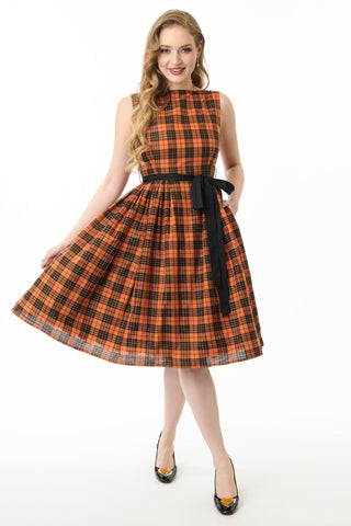 Model wearing a cotton orange, black, and yellow gold lurex plaid patterned swing dress with slash neckline, darted bodice, black cotton sash belt, and below the knee gathered skirt. Shown from front with skirt held out