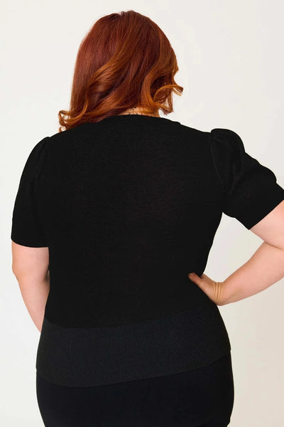 Model wearing black knit pullover sweater with round neckline, slightly puffed balloon short sleeves, wide ribbed bottom band, and jacquard knit image across bust of a stylized moth in black, white, grey, and teal. Shown from back