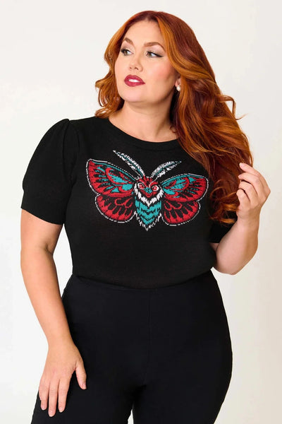 Plus size model wearing black knit pullover sweater with round neckline, slightly puffed balloon short sleeves, wide ribbed bottom band, and jacquard knit image across bust of a stylized moth in black, white, grey, and teal. Shown from front