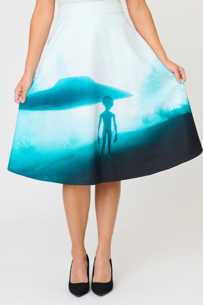 high waisted woven swing skirt with all-over photo print in shades of blue of alien in front of floating flying saucer. Skirt has side seam pockets and ends at the knee. Shown on model from front in close up of skirt 