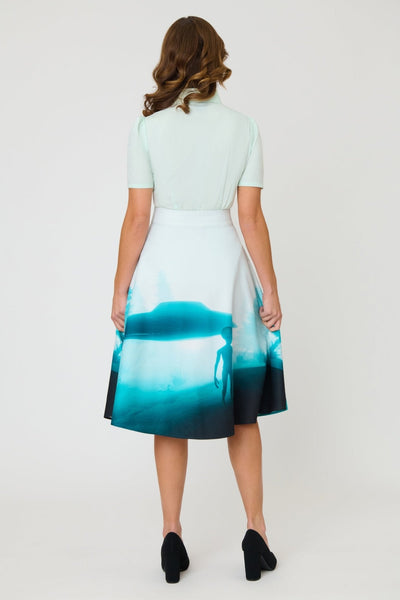 high waisted woven swing skirt with all-over photo print in shades of blue of alien in front of floating flying saucer. Skirt has side seam pockets and ends at the knee. Shown on model from back