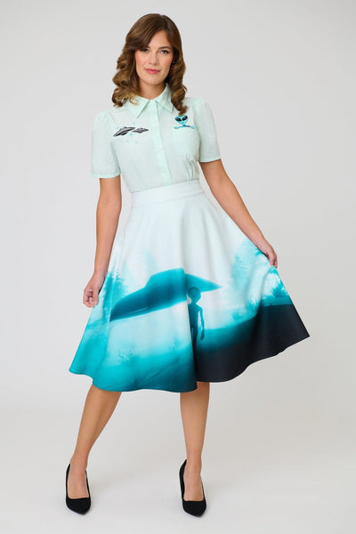 high waisted woven swing skirt with all-over photo print in shades of blue of alien in front of floating flying saucer. Skirt has side seam pockets and ends at the knee. Shown on model from front
