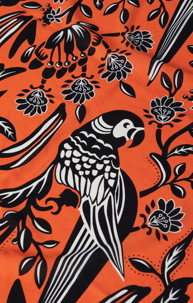 Vintage inspired semi-sheer black, orangey red and white chiffon square scarf in a floral pattern with a black and white parrot. Seen in close up for pattern detail
