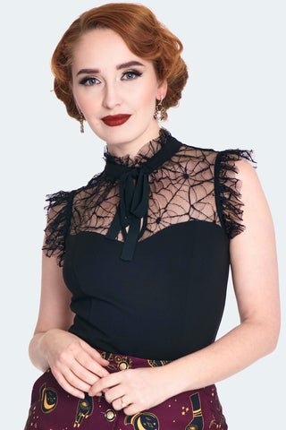 A model wearing a black sleeveless spider patterned lace top with a solid black knit bodice. It has a high frilly lace neck and matching black tie at the collar with a keyhole detail. Shown from front 