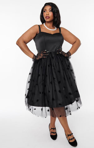 A model wearing a black swing dress with a sweetheart neckline, princess seaming, and matching spaghetti straps. The skirt is full and just below the knee and has a black tulle overlay with an all-over pattern of flocked black cockroaches. Seen from front 
