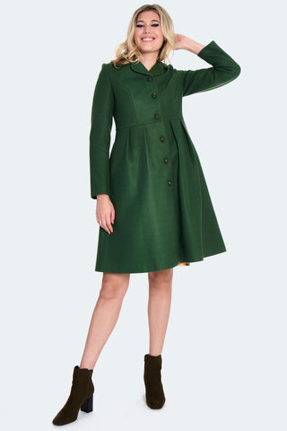 A model wearing a forest green 60s style coat with a wide collar, matching color floral buttons down the front, princess seaming at the bodice, and pleating at the waist. It ends just above the knee. Shown buttoned up from the front 