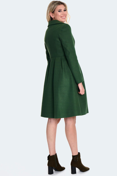 A model wearing a forest green 60s style coat with a wide collar, matching color floral buttons down the front, princess seaming at the bodice, and pleating at the waist. It ends just above the knee. Shown buttoned up from the back