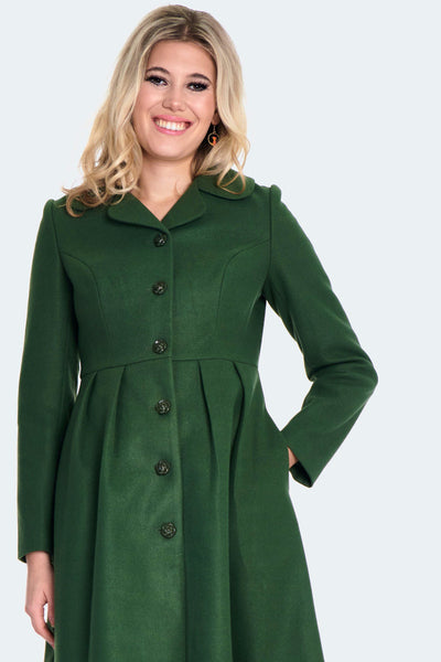 A model wearing a forest green 60s style coat with a wide collar, matching color floral buttons down the front, princess seaming at the bodice, and pleating at the waist. It ends just above the knee. Shown buttoned up from the front in close up