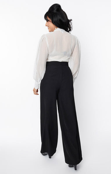 Model wearing high waisted black trousers with a wide cummerbund style waist and wide legs. Shown from back