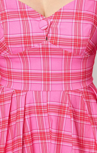 Model wearing a swing dress in a pink, red, and white plaid pattern with 3/4 sleeves, sweetheart neckline with button detail, open square back, and a full knee length skirt. Shown in close up for pattern detail